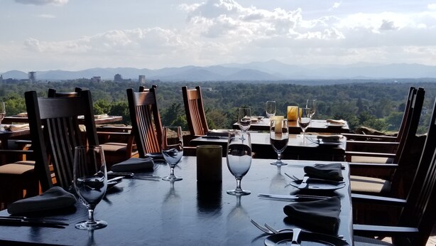 Une table de restaurant dressée avec des verres à vin, des assiettes et des couverts, donnant sur un paysage montagneux.