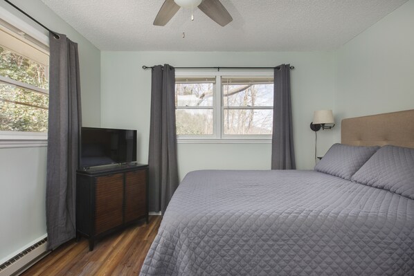 A bedroom with a bed, a dresser, a television, a window with curtains, and a ceiling fan.