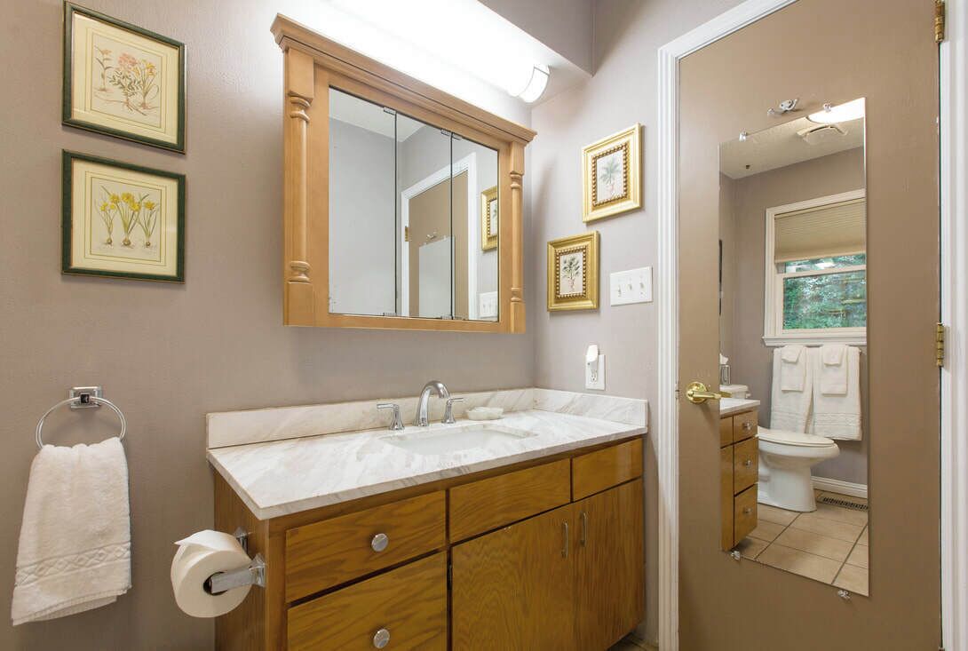 A bathroom with a wooden vanity, a large mirror, and framed botanical prints on the wall.