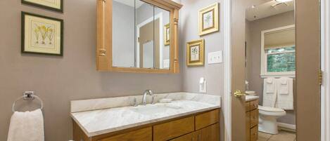 A bathroom with a wooden vanity, a large mirror, and framed botanical prints on the wall.