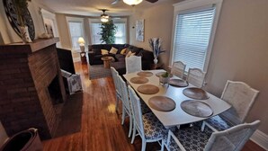 A dining area with a long table, white chairs, and a ceiling fan.