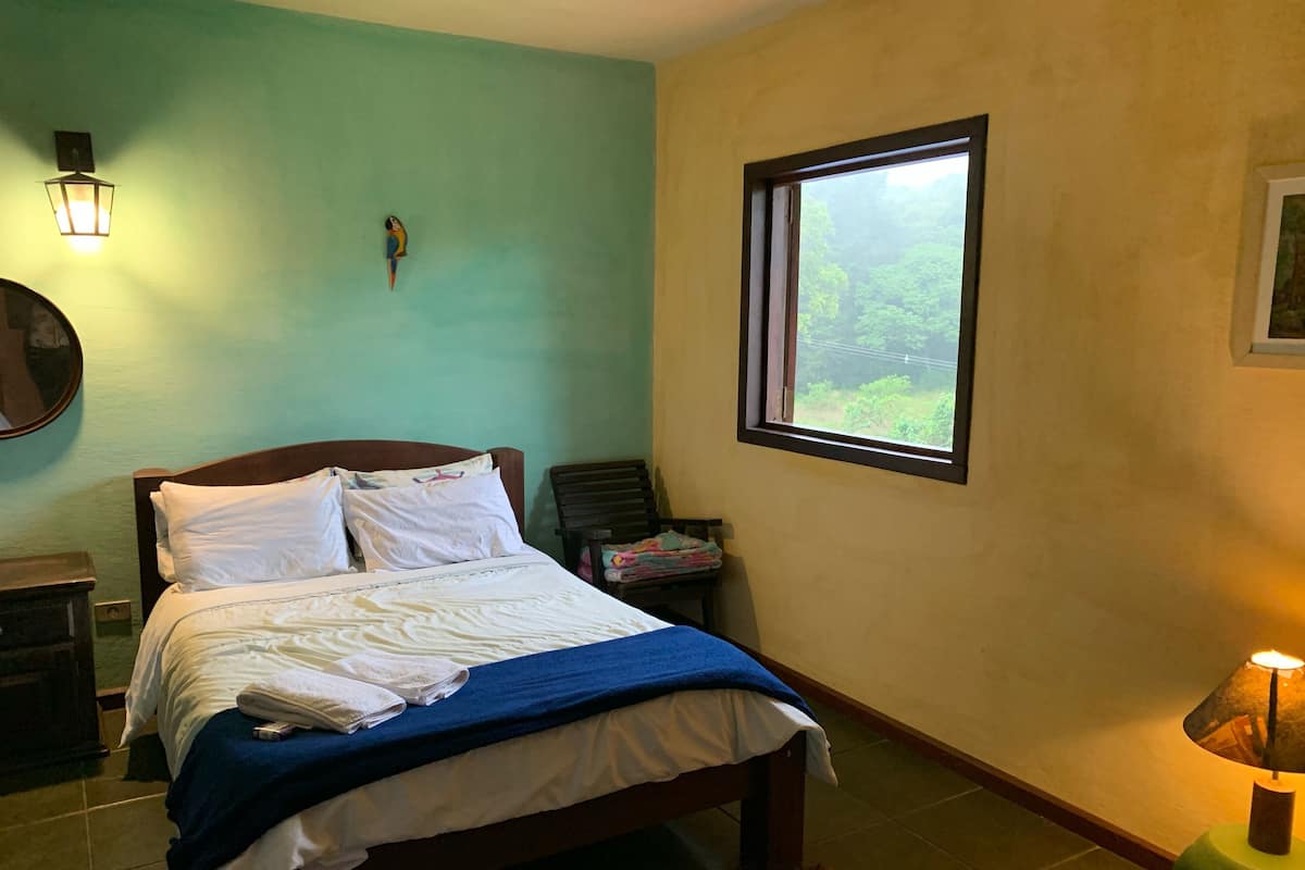 A bedroom with a bed, a nightstand, a lamp, a window, and a wall-mounted light fixture.