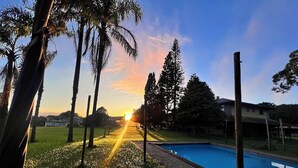 A swimming pool with a grassy area and trees in the background. - Pousada Refúgio Dinamarca (Mairipora)