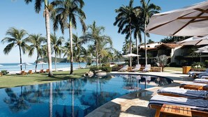 A poolside area with lounge chairs, palm trees, and a view of the ocean.
