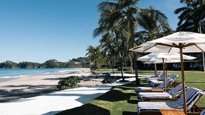 A beach resort with sun loungers, umbrellas, and palm trees.