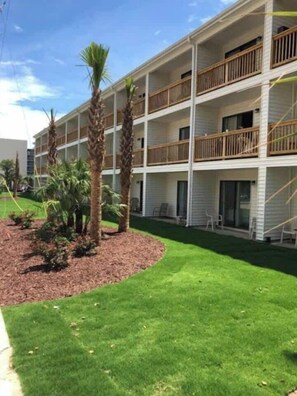 Un hotel de varios pisos con balcones, un césped cuidado y palmeras.