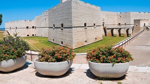 Une forteresse historique en pierre, dotée d’une tour centrale, entourée d’une pelouse bien entretenue et de grands jardinières fleuries.