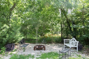Relax in a serene garden setting with a fire pit, bench, and lush greenery.