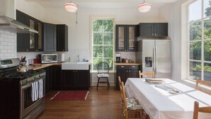 A kitchen with dark cabinets, a stainless steel stove, a microwave, and a refrigerator. There is a window with a view of greenery outside.