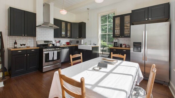 A modern kitchen with dark cabinets, stainless steel appliances, and a dining area with a table and chairs.