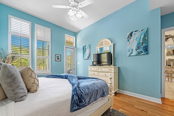 A bedroom with a bed, a dresser, a ceiling fan, and artwork on the walls.