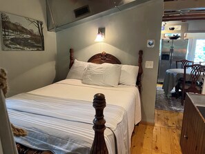 Un dormitorio con cama de madera, una mesita de noche, una lámpara, un cuadro en la pared y vistas al área de la cocina.