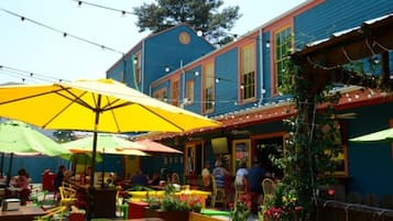 An outdoor seating area with colorful umbrellas and tables, surrounded by a building with blue siding and red trim.