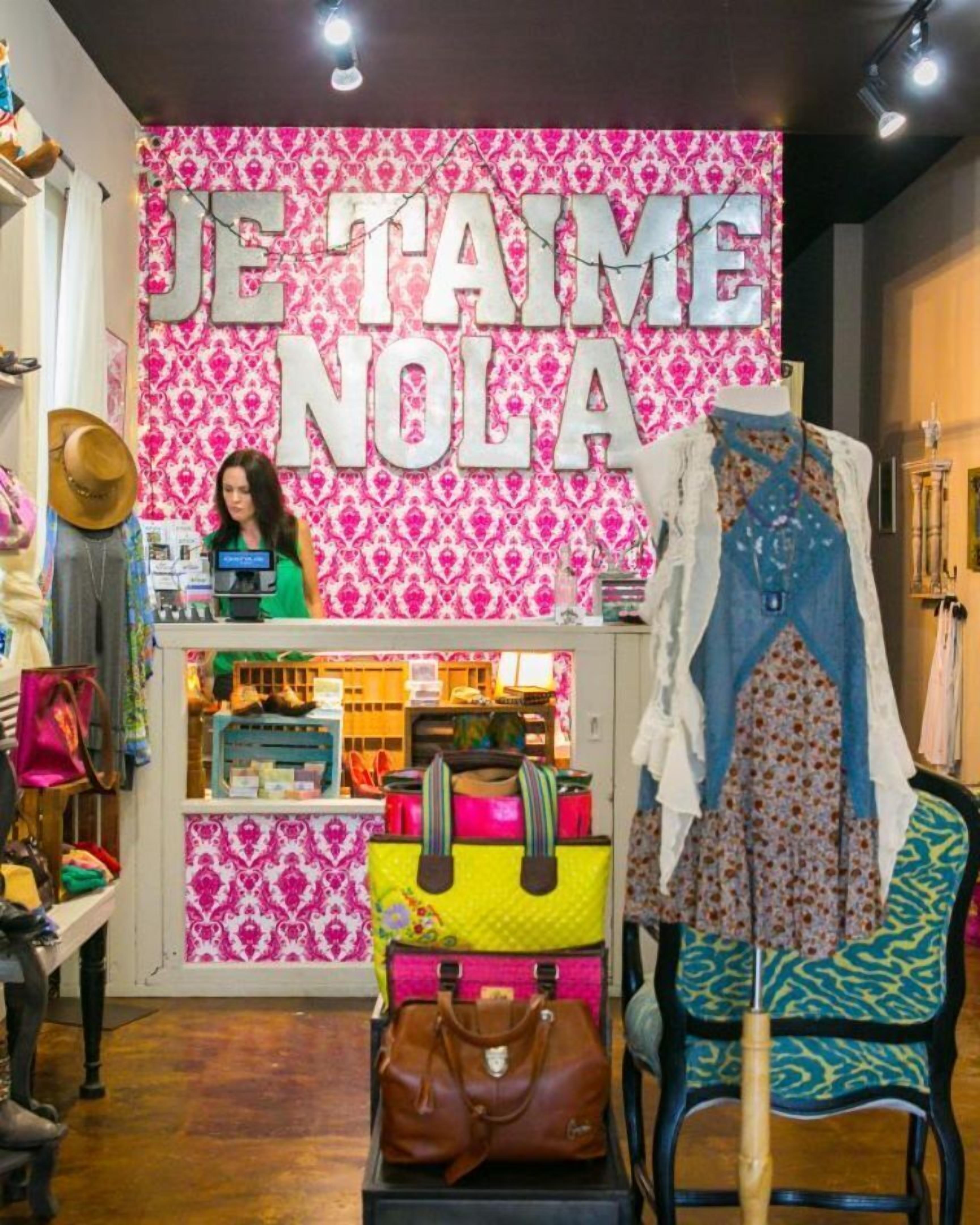 Een boetiek met een levendige roze- en witgestreepte wand, een etalagemodel dat een blauwe jurk draagt, en diverse handtassen.