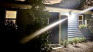 Una casa con techo inclinado, una ventana a la vista y un pequeño jardín con grava y plantas en macetas.