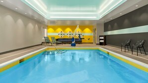 Una piscina interior con superficie de agua cristalina, rodeada de sillas de descanso y una mesa junto a la piscina.