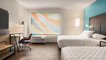 Een hotelkamer met een bed, een bureau, een stoel, een staande lamp en een kleurrijk abstract schilderij aan de muur.
