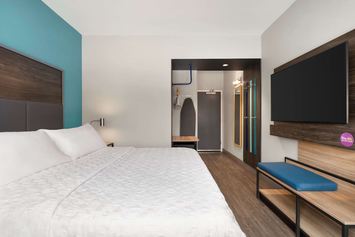 Een moderne hotelkamer met een groot bed, een bankje, een flatscreen televisie en een kledingkast.