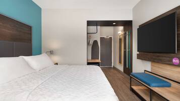 Una habitación de hotel moderna con una cama grande, un banco, un televisor de pantalla plana y un armario.