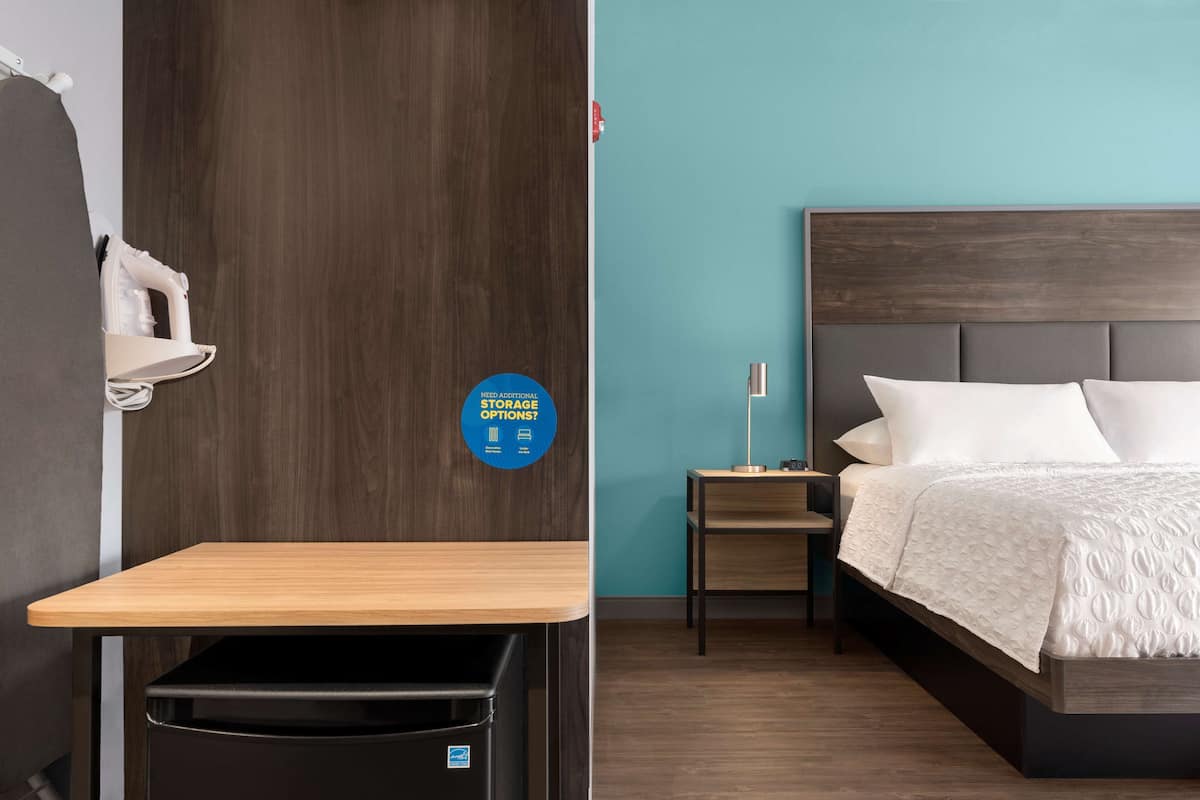 Een hotelkamer met een bed, nachtkastje, bureau en een prullenbak.