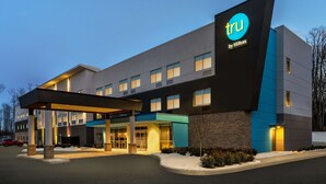 Un hotel moderno con un llamativo letrero de 'tru by Hilton', un acceso cubierto y un estacionamiento.