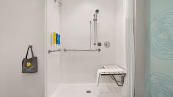 Eine bodenebene Dusche mit Sitzbank, Handtuchhalter und Händedesinfektionsspender.