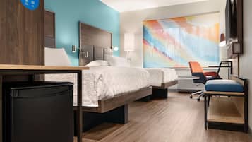 Une chambre d’hôtel avec deux lits, un bureau, une chaise, un réfrigérateur et un grand tableau abstrait accroché au mur.