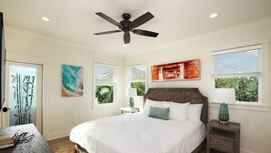 A bedroom with a large bed, a ceiling fan, and artwork on the walls.