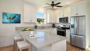 A modern kitchen with white cabinets, a stainless steel refrigerator, a microwave, and a ceiling fan.