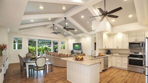 A modern kitchen with white cabinetry, a central island, and built-in appliances. - Hale Lo'i + Cottage: 5BR home +pool in Sunny Poipu (Koloa)