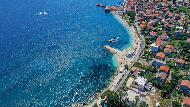 Vista aérea de un pueblo costero con playa, barcos y un muelle.