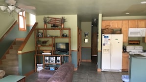 A living room with a brown leather couch, a TV, and a wooden entertainment unit with shelves and speakers.