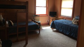 A bedroom with bunk beds, a desk with a computer, and two windows with blinds.