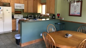A kitchen with wooden cabinets, a white refrigerator, a microwave, a stove, and a dining area with a wooden table and chairs.