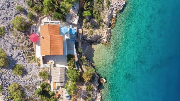 Luchtbeeld van een kustbezit met een huis, een zwembad en helder turquoise water.