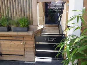 Una escalera de madera que conduce a un entrepiso identificado con 'LE LOFT', con plantas en macetas en la plataforma.