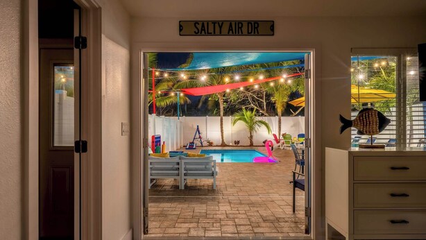 An entrance to a pool area with a sign reading "SALTY AIR DR", a pool, a bench, and a decorative fish sculpture. - Coconut Dreams! Heated Pool, 4 min to AMI Beach (Bradenton)