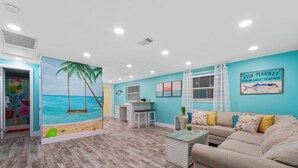 A living room with a beach mural, a kitchenette, a sofa, and a dining table. - Coconut Dreams! Heated Pool, 4 min to AMI Beach (Bradenton)