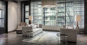 A modern living room with a sofa, armchairs, and a coffee table. There are large windows with a view of buildings and trees. - Harbor Steps (Seattle)