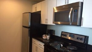 Una cocina compacta con gabinetes blancos, un refrigerador negro, un microondas de acero inoxidable y una estufa negra.