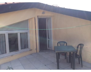 Una piccola zona patio con tavolo e sedie, una porta scorrevole in vetro e un pavimento piastrellato.