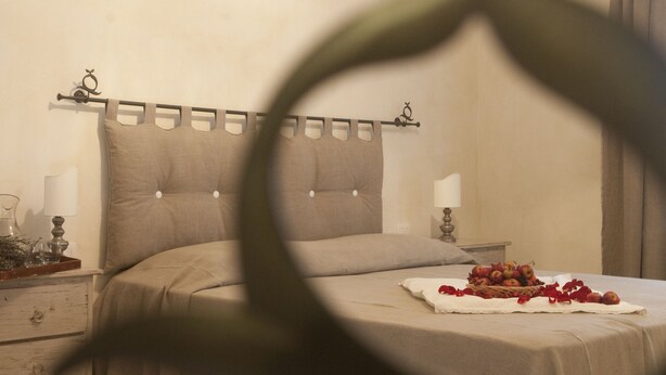 A neatly made bed with a headboard, a bedside table with a lamp, and a basket of fruit on the bed. - Rinidia Siena Celso Cittadini Grande (Siena)