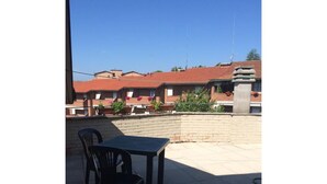 An outdoor patio area with a table and chairs, a brick wall, and buildings in the background. - Rinidia Siena Celso Cittadini Grande (Siena)