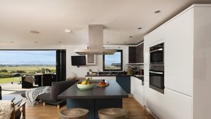 A modern kitchen with a central island, built-in oven, and a large window offering a view of the outdoors. - A stunning two bedroom eco-home with breath-taking countryside views. (Chapel Porth)