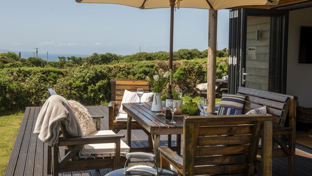 Une terrasse extérieure avec des meubles en bois, un grand parasol et une vue sur la mer.
