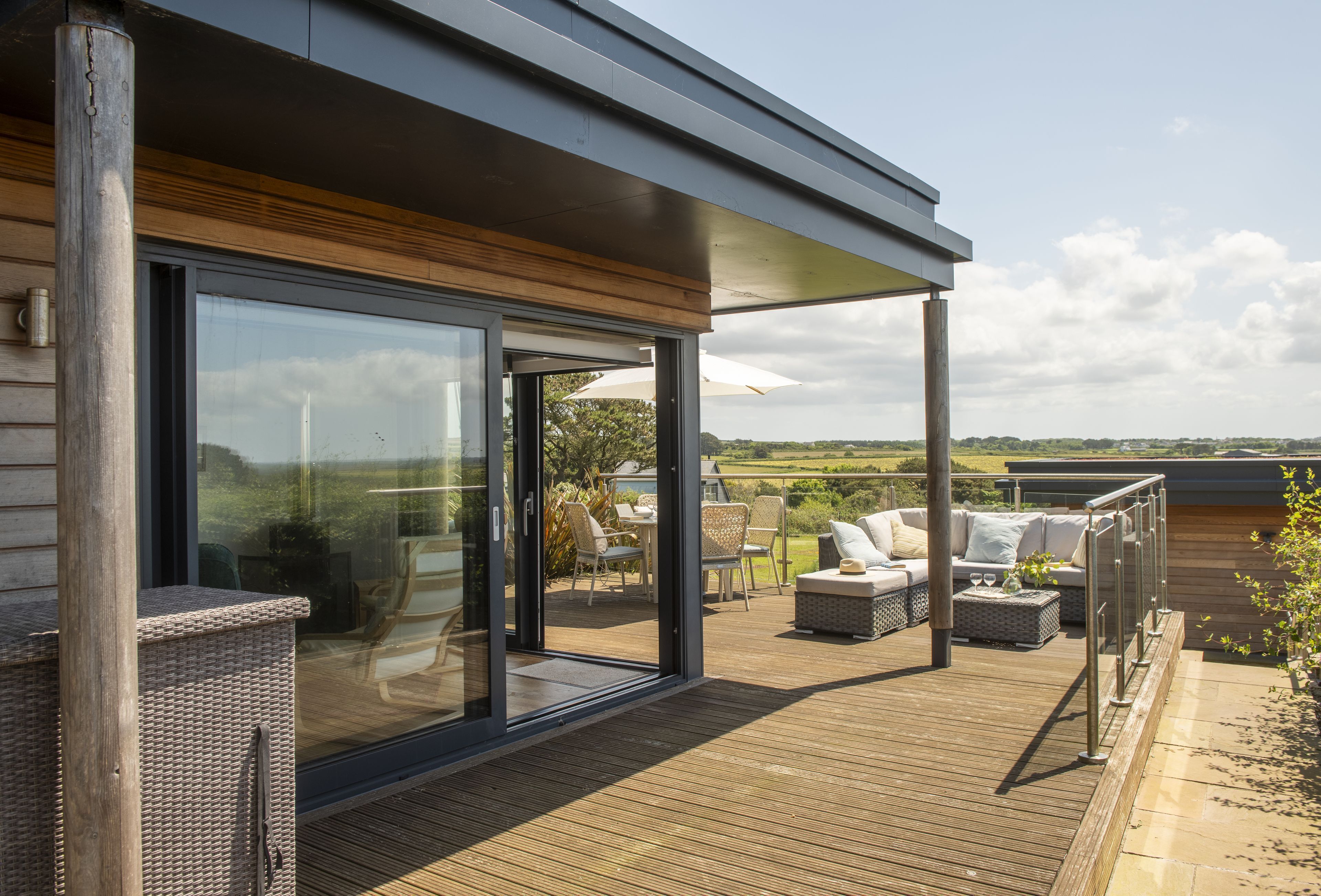 Eine moderne Außenterrasse mit Glastüren, die auf eine Patio mit Gartenmöbeln und Blick ins Grüne führt.