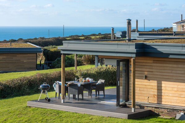 Ein moderner Essbereich im Freien mit Blick aufs Meer, ein Grill und ein Holzgebäude.