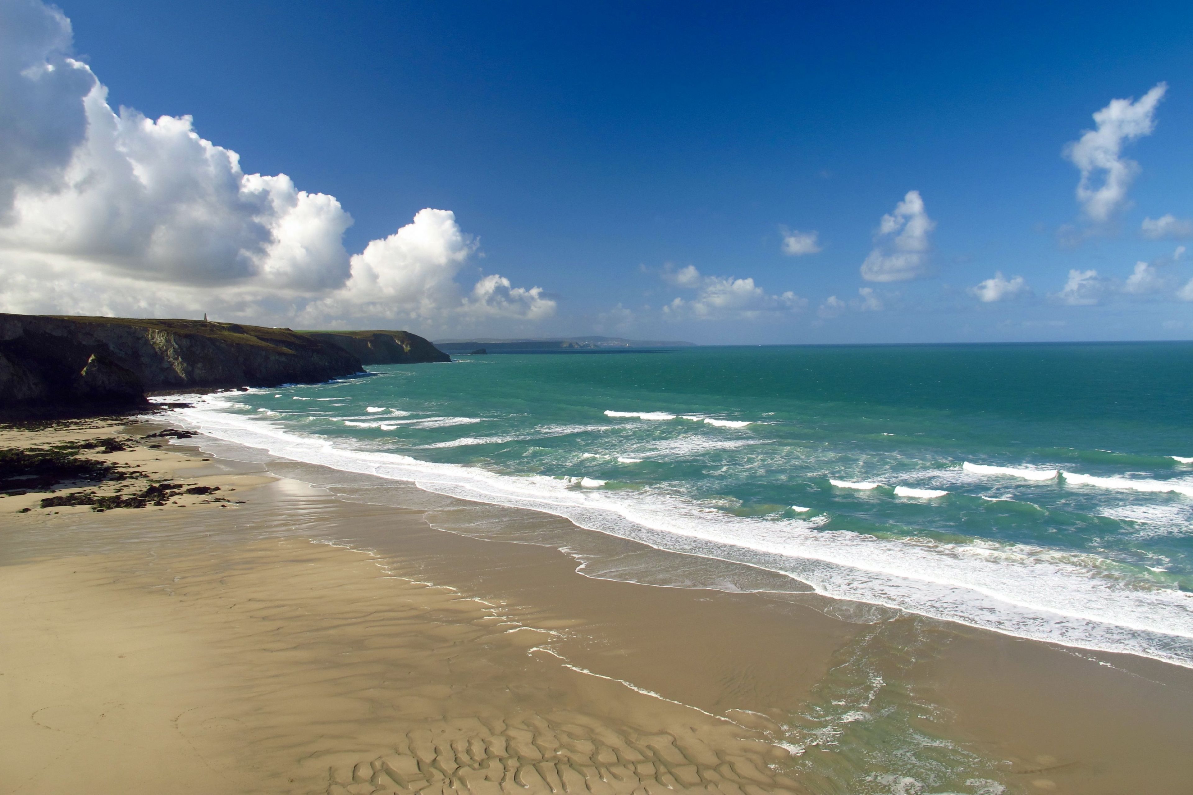 A beach with a clear view of the ocean and a rocky cliff.