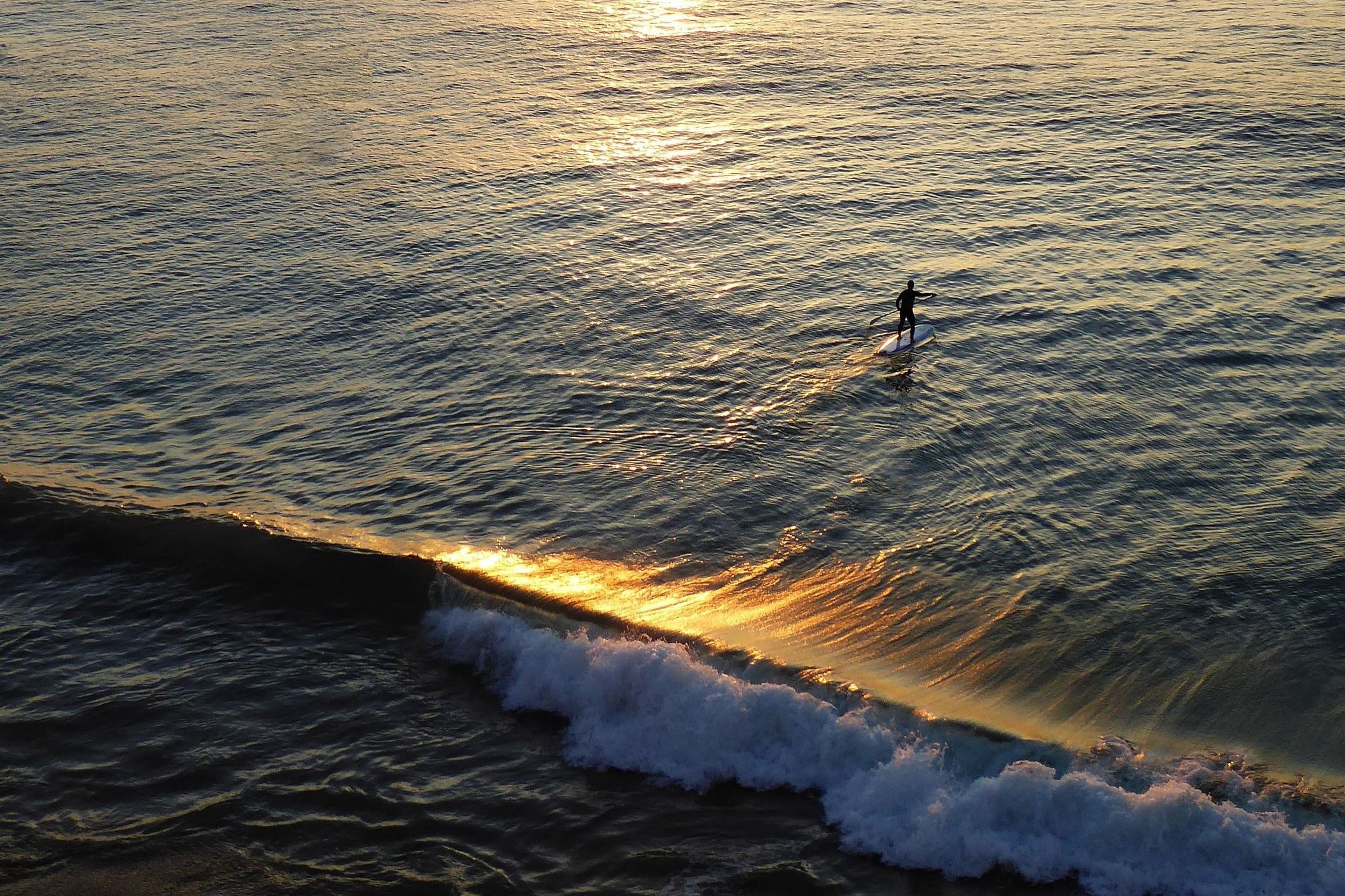 Una persona surfeando una ola con el sol poniéndose en el fondo.