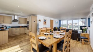 A modern kitchen with wooden cabinets, a dining table set for six, and a large window offering a view of the outside. - A superbly situated property that is just a short walk from two fabulous beaches (Newquay)